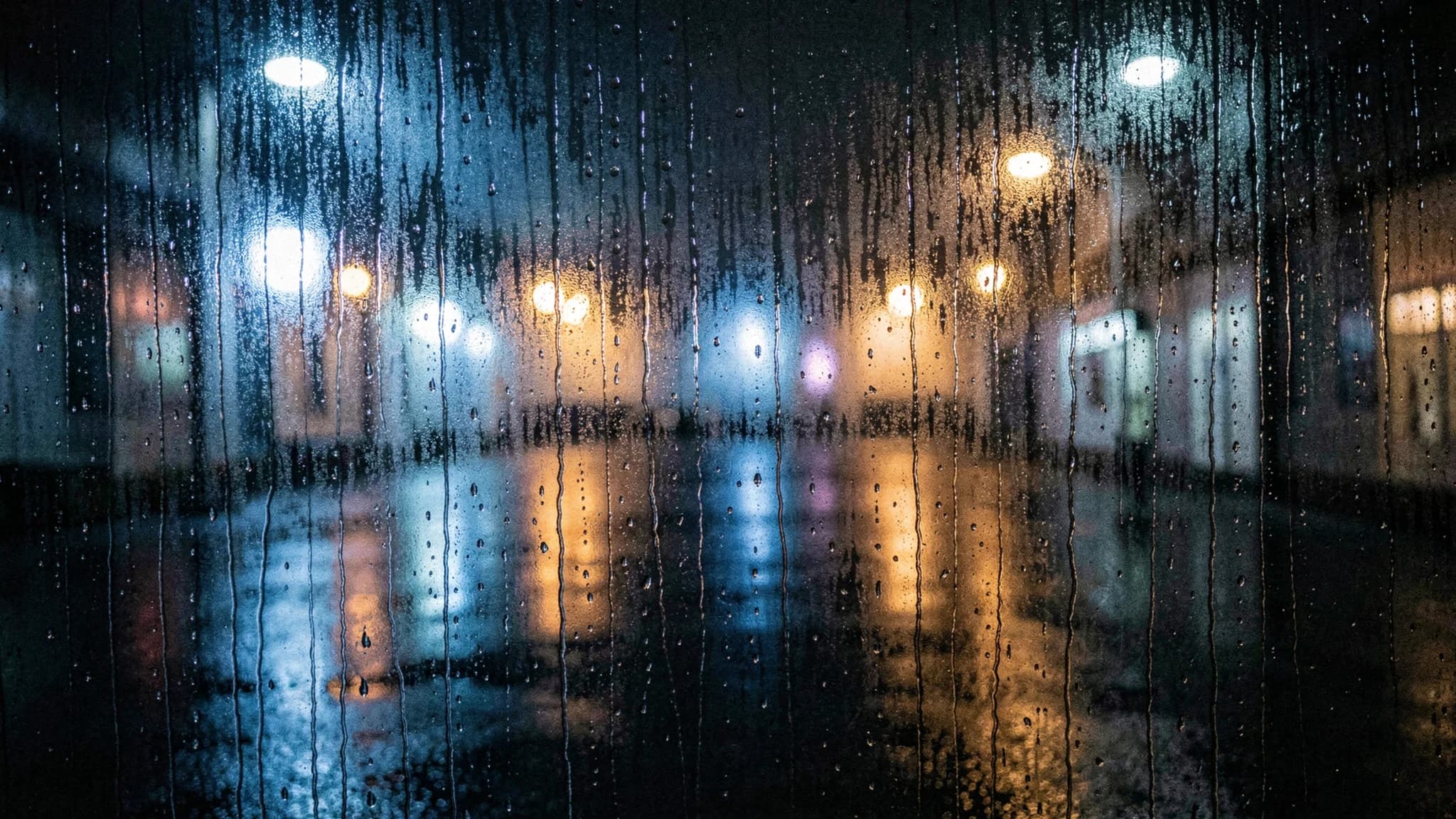 Regendruppels op donker vensterglas met vervaagde achtergrondlichten