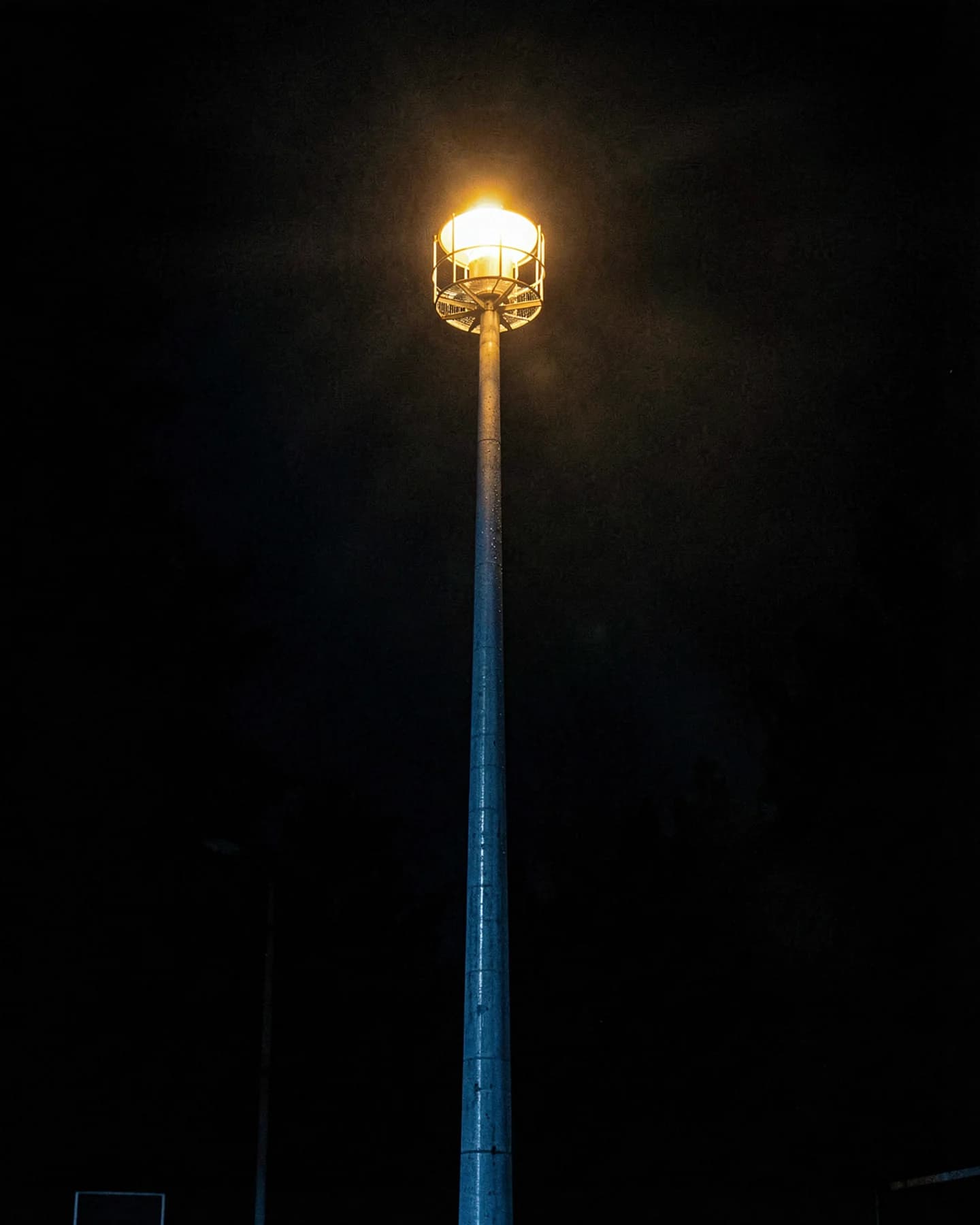 Hoge lichtmast met felle schijnwerper tegen een zwarte nachthemel