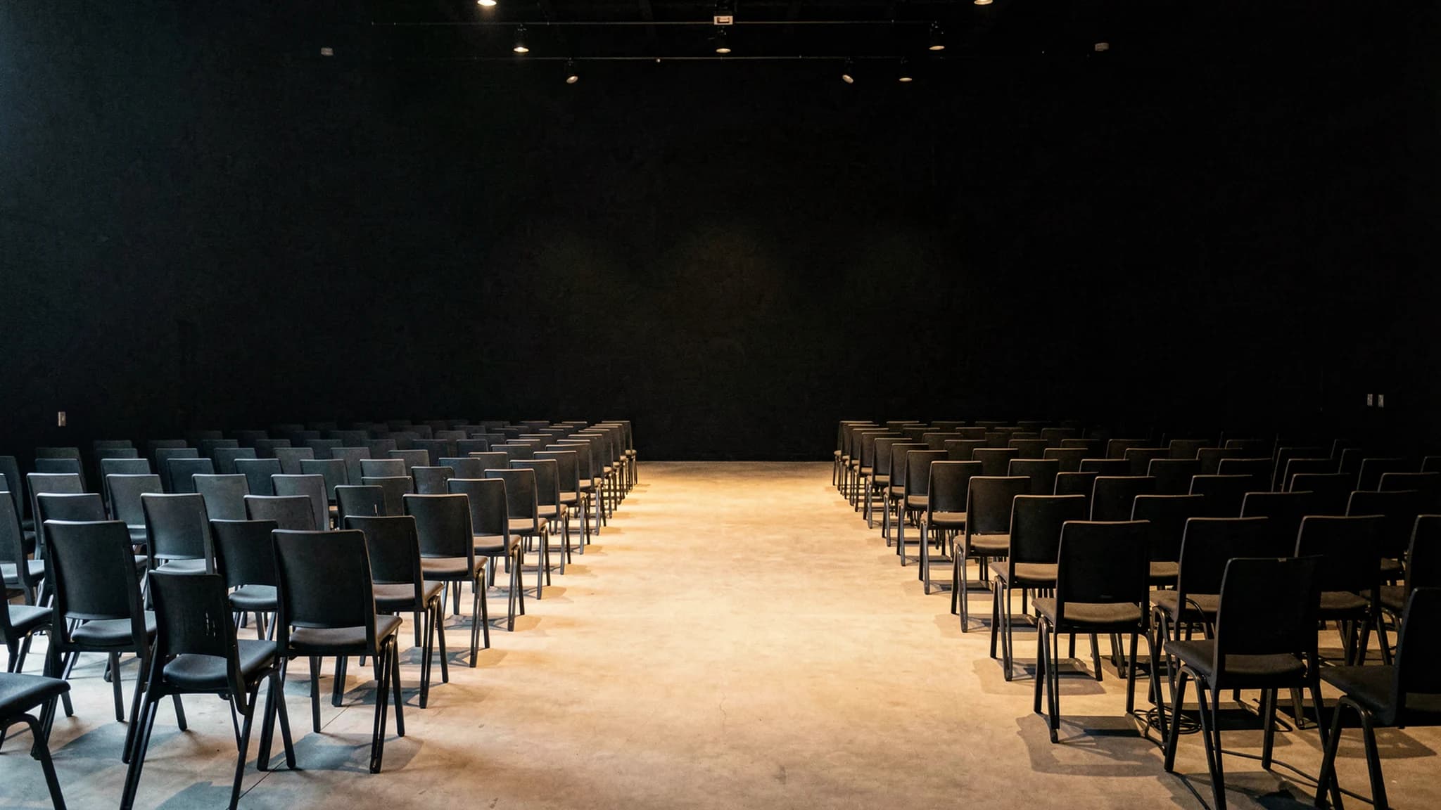 Zaal met strakke rijen stapelstoelen en laag daglicht