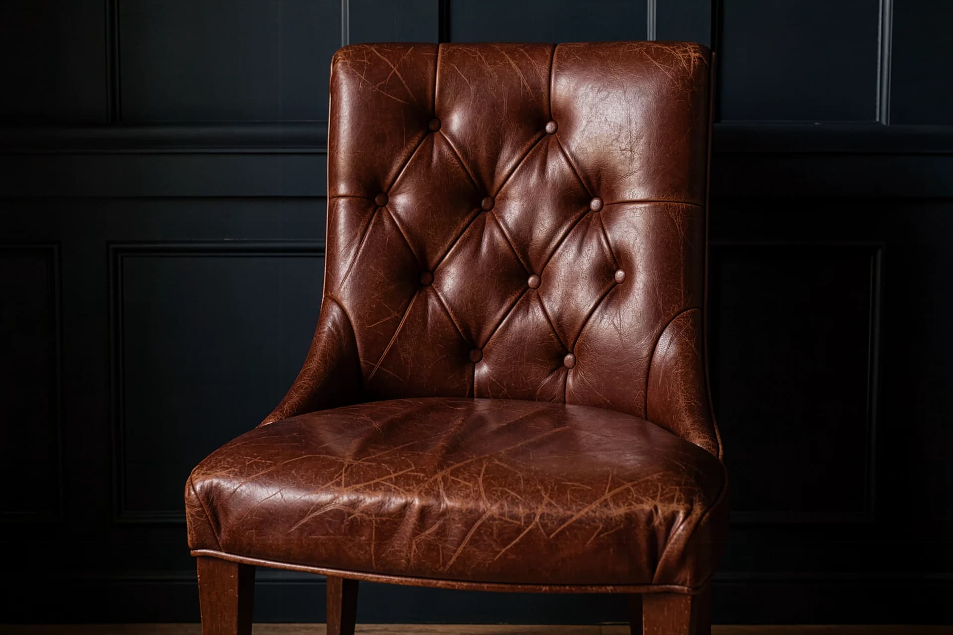 Gecapitonneerde ossenbloedrode leren fauteuil voor donkere lambrisering
